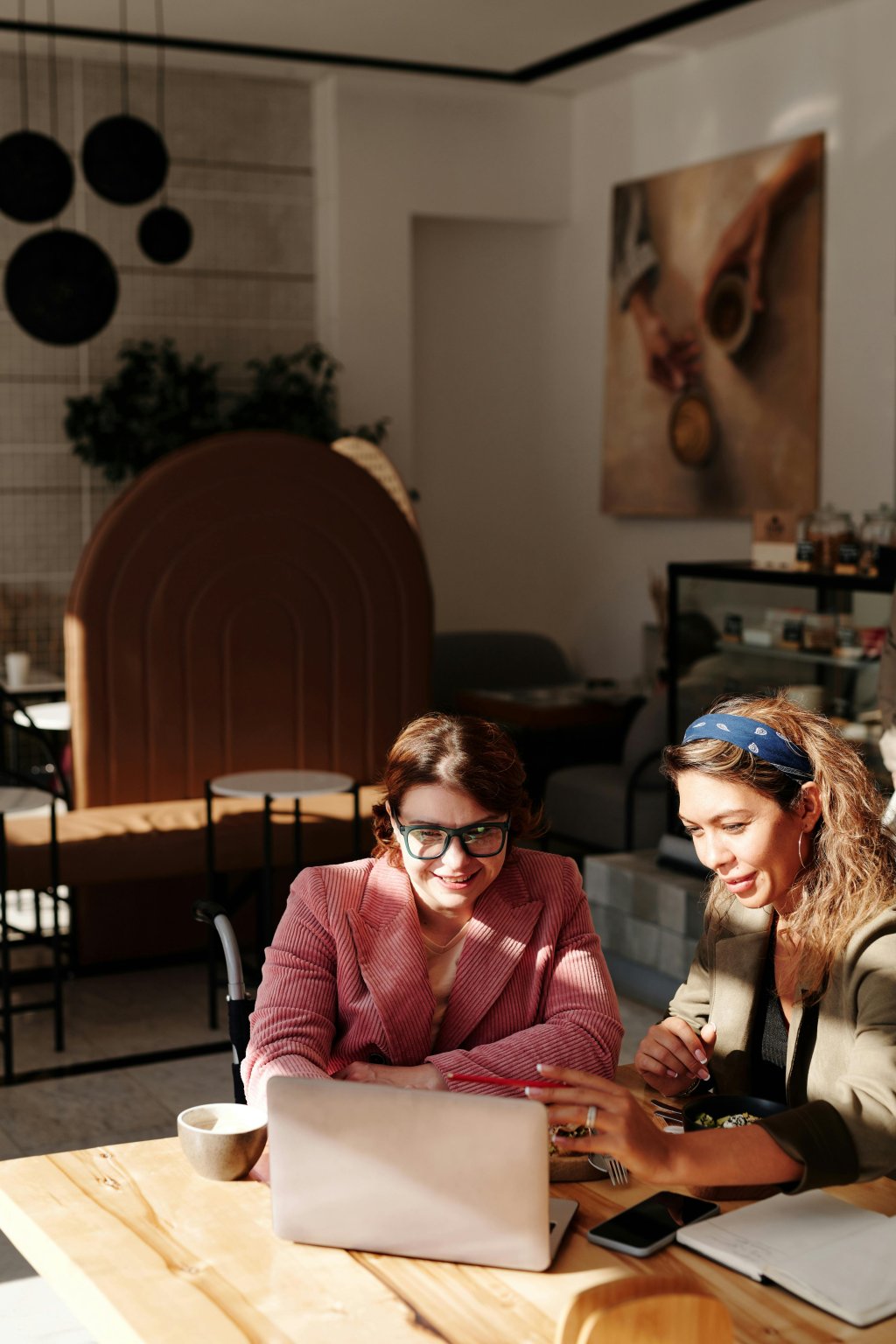 Two women working together on a laptop in a modern office or cafe. One is in a wheelchair.