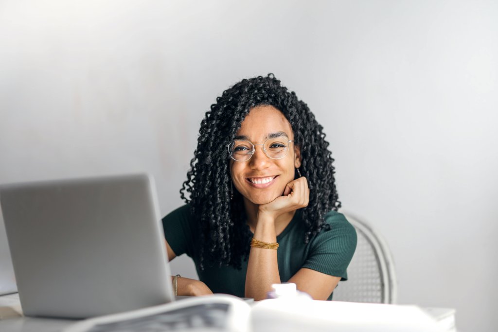 Photo of a smiling young black woman sitting at a laptop.